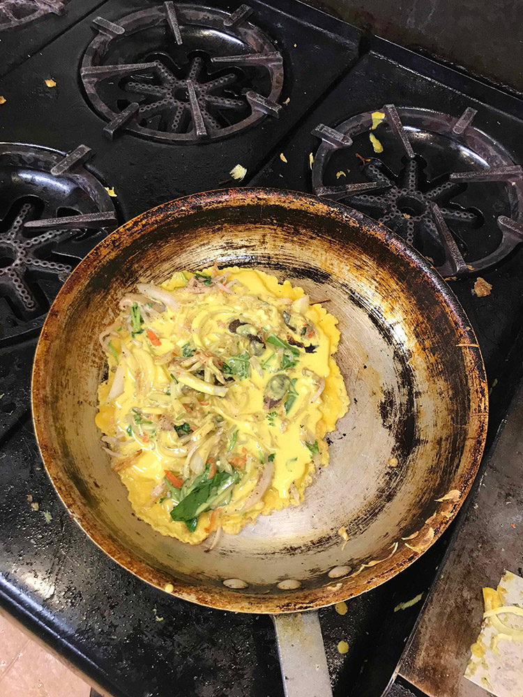 egg yolk crepe cooking on skillet with shredded vegitables inside