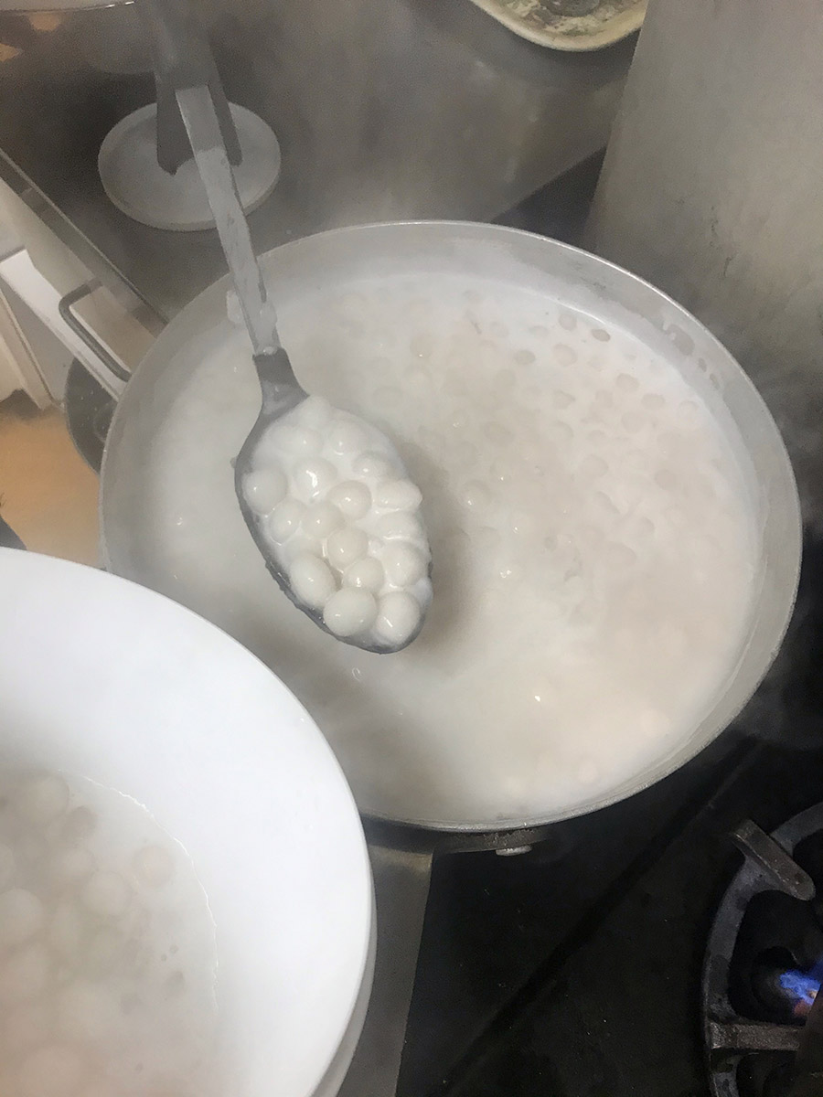a spoon full of small pearls of tapioca in the saucepan of chè khoai lang