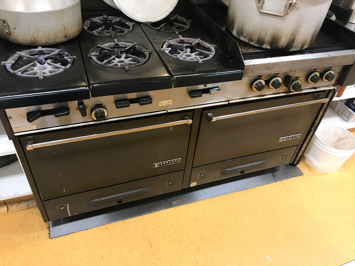an industrial gas cooker with 6 stove tops, one griller and two large ovens. there are 2 big aluminum pots on the stoves.