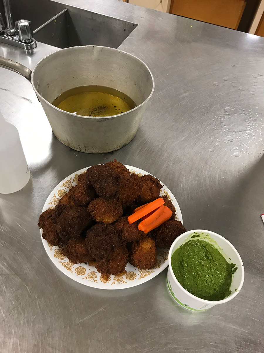 20 or so fresh fried falafels on a plate, with a green dipping suace next to it. the fry oil is cooling in the background on the same surface