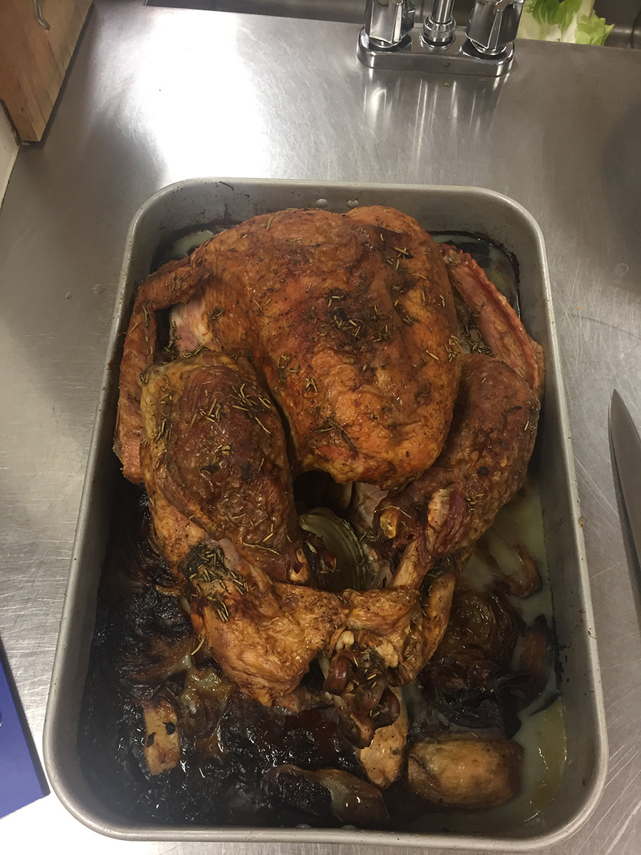 a roasted turkey with browned onions on lots of fat on the bottom of the pan