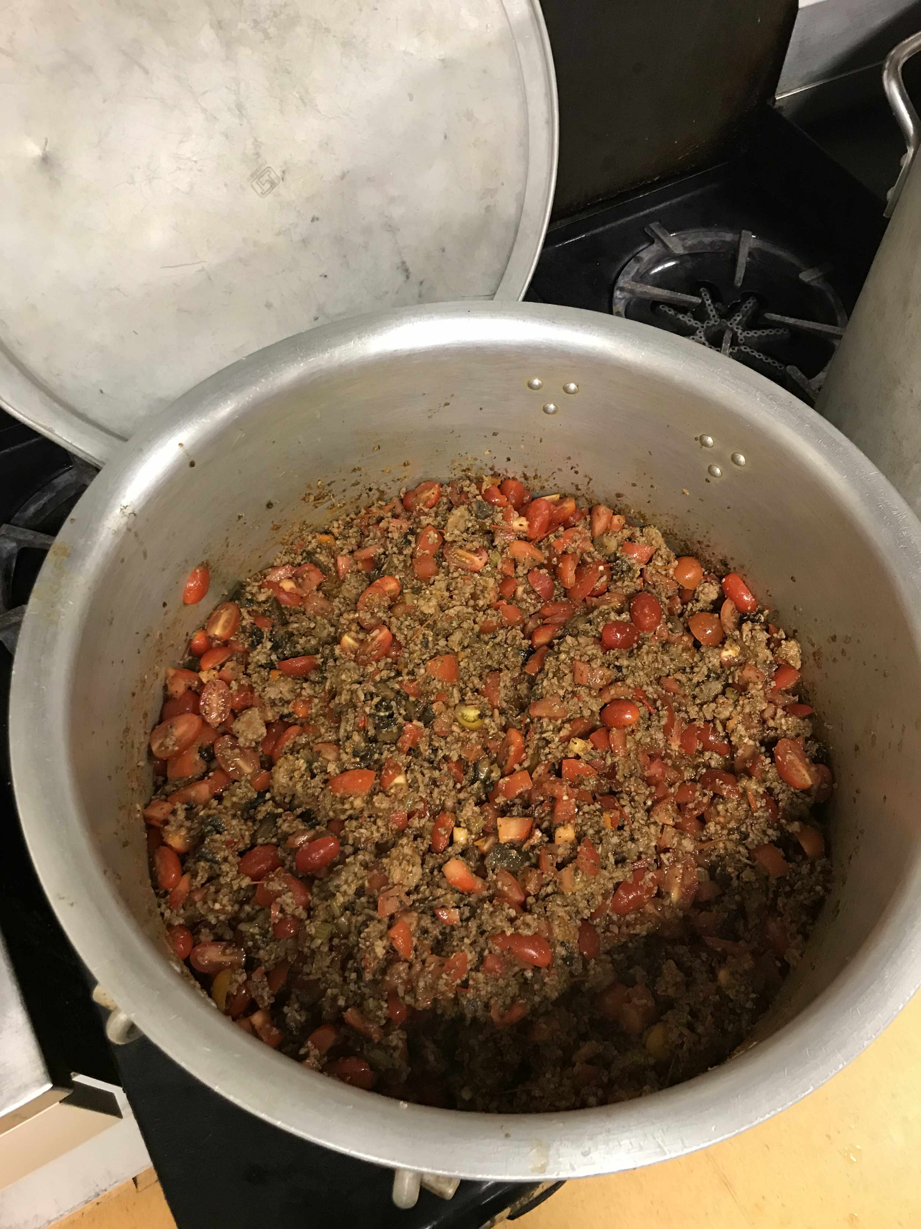minced meat with fresh cherry tomatoes halved in a 40 litre pot, seasoned with herbs. to be used for bolognese sauce.