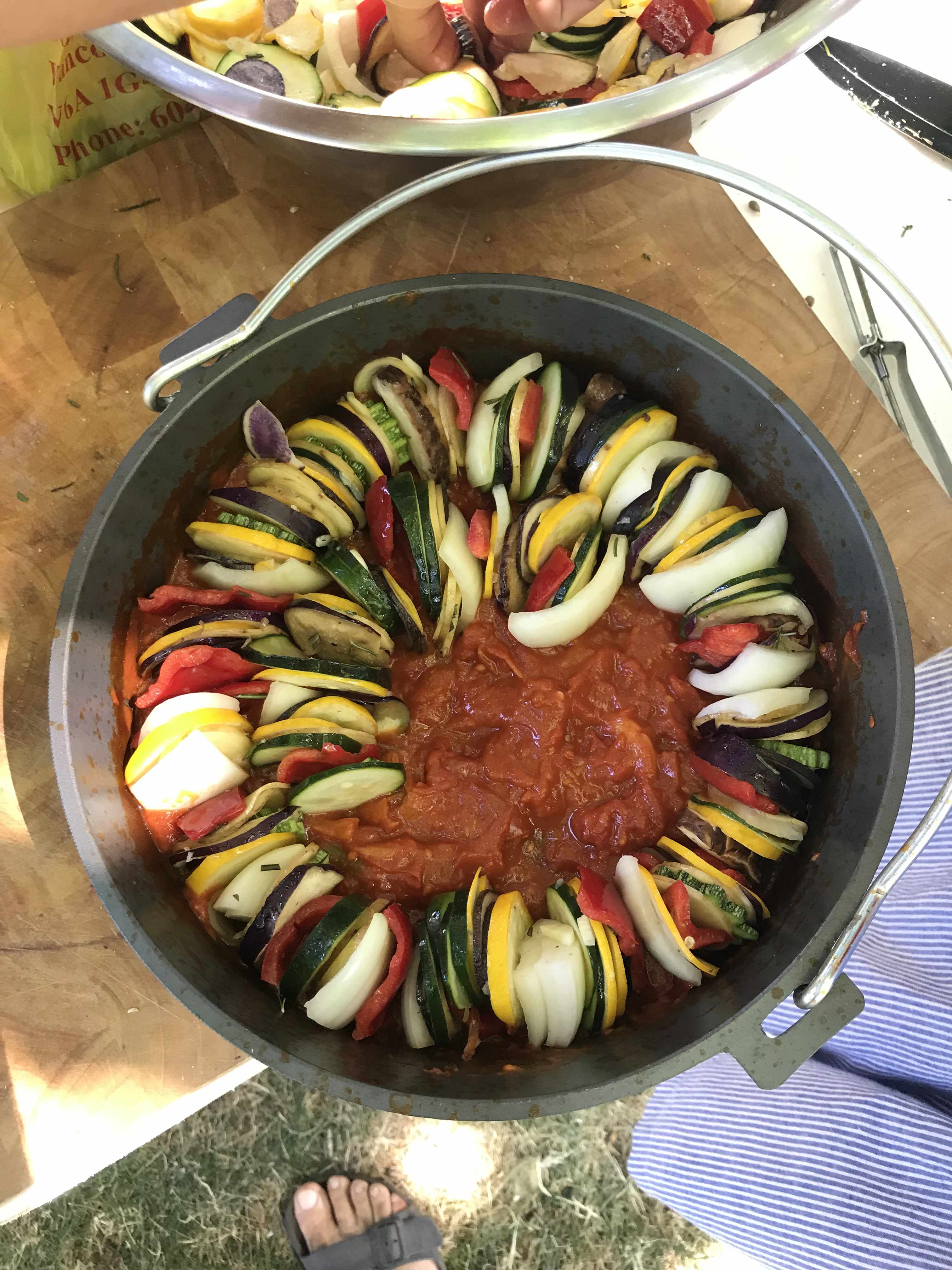 an iron cast pan full of thinliy sliced onion, zucchini, eggplant, and peppers, shaped in a spiral and tomato sauce in the middle.