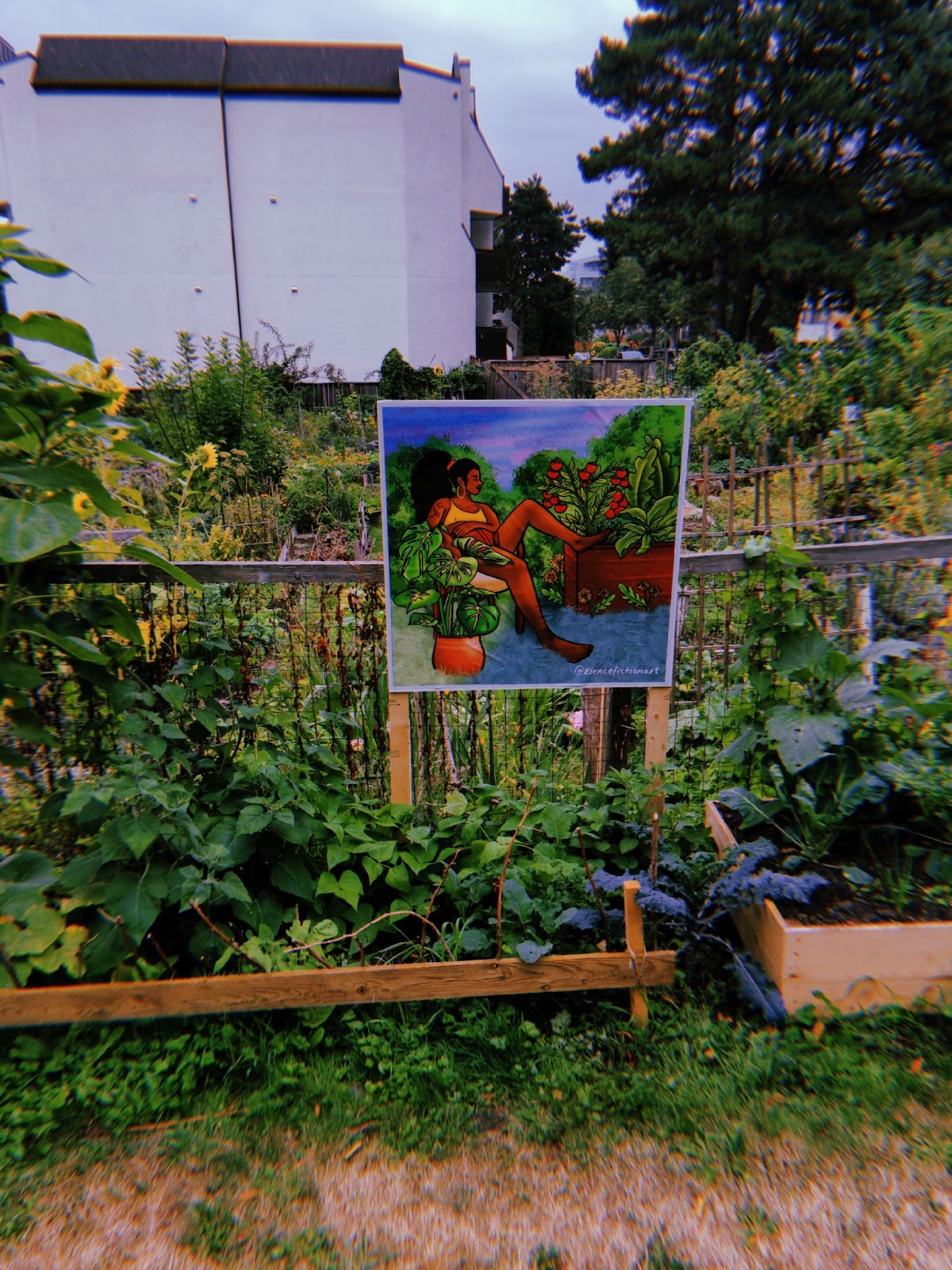 a painting of a person lounging in a garden, installed along the fence of a community garden