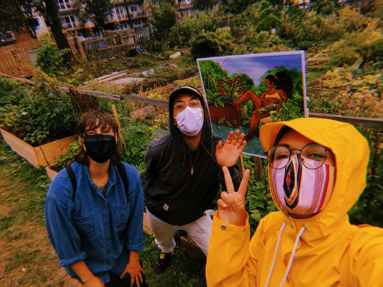 three people (Vivienne, Derya, and Zion) posed besides a painting inside a community garden