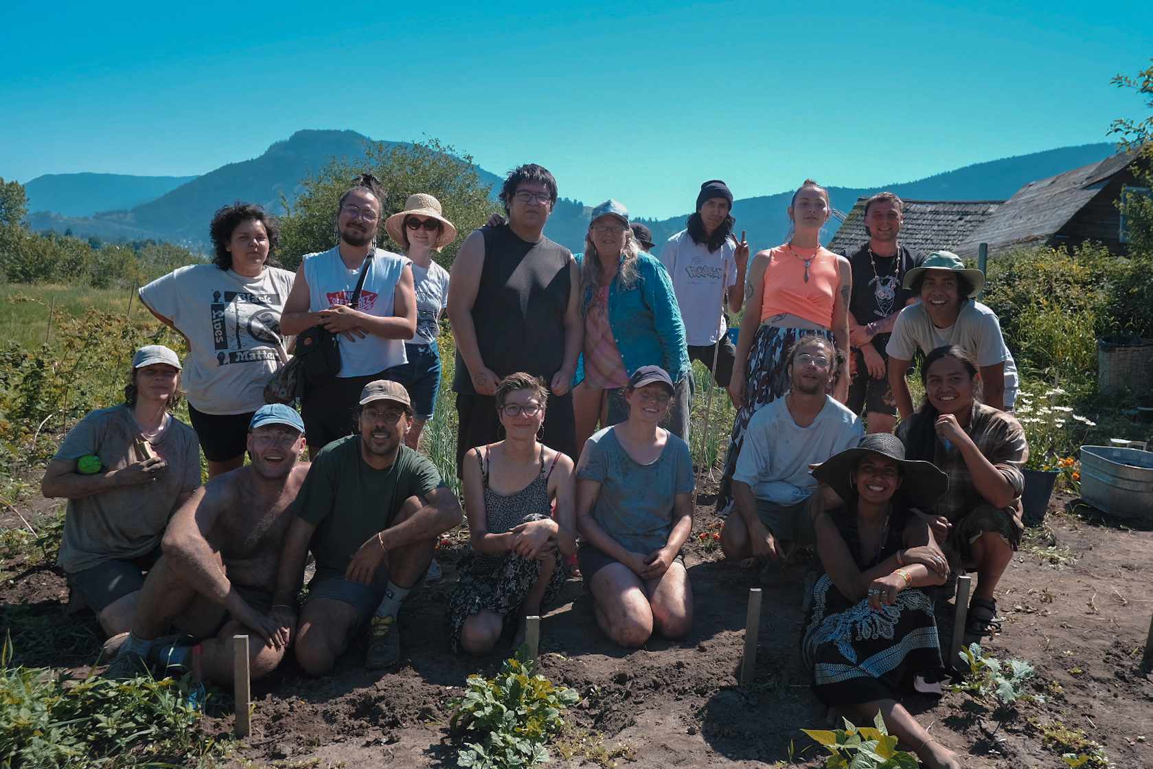 A group of people, one row kneeling and one row standing, pose in a garden with a mountain range behind them
