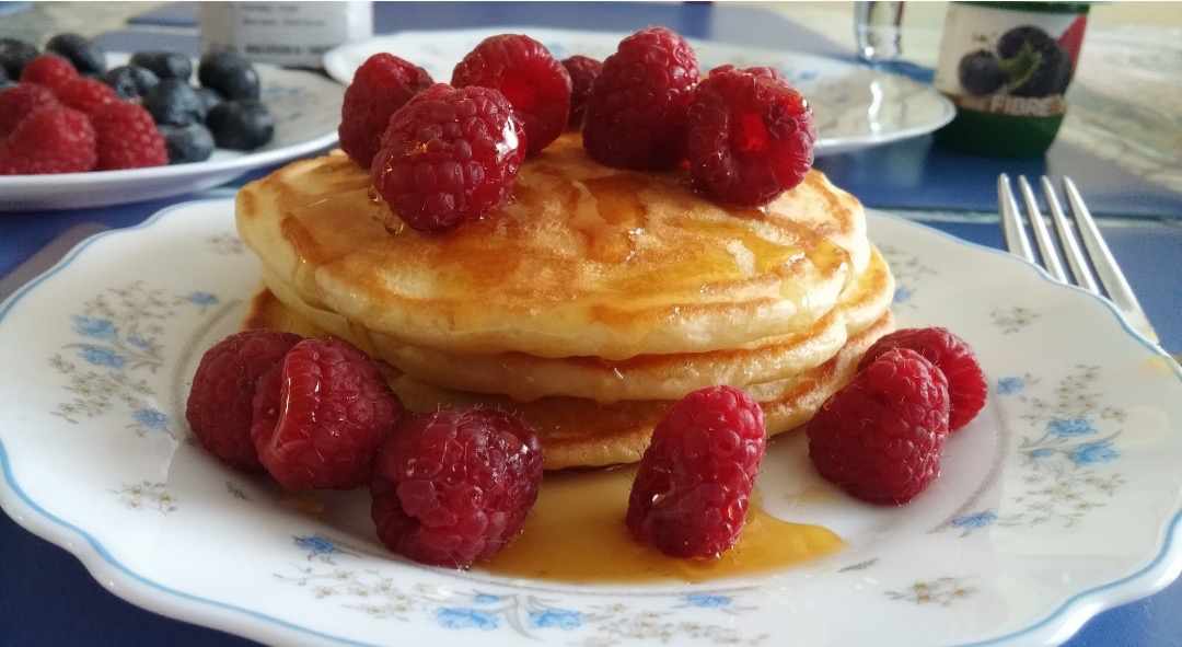 plate of pancakes with maple syrup and lots of raspberries on top