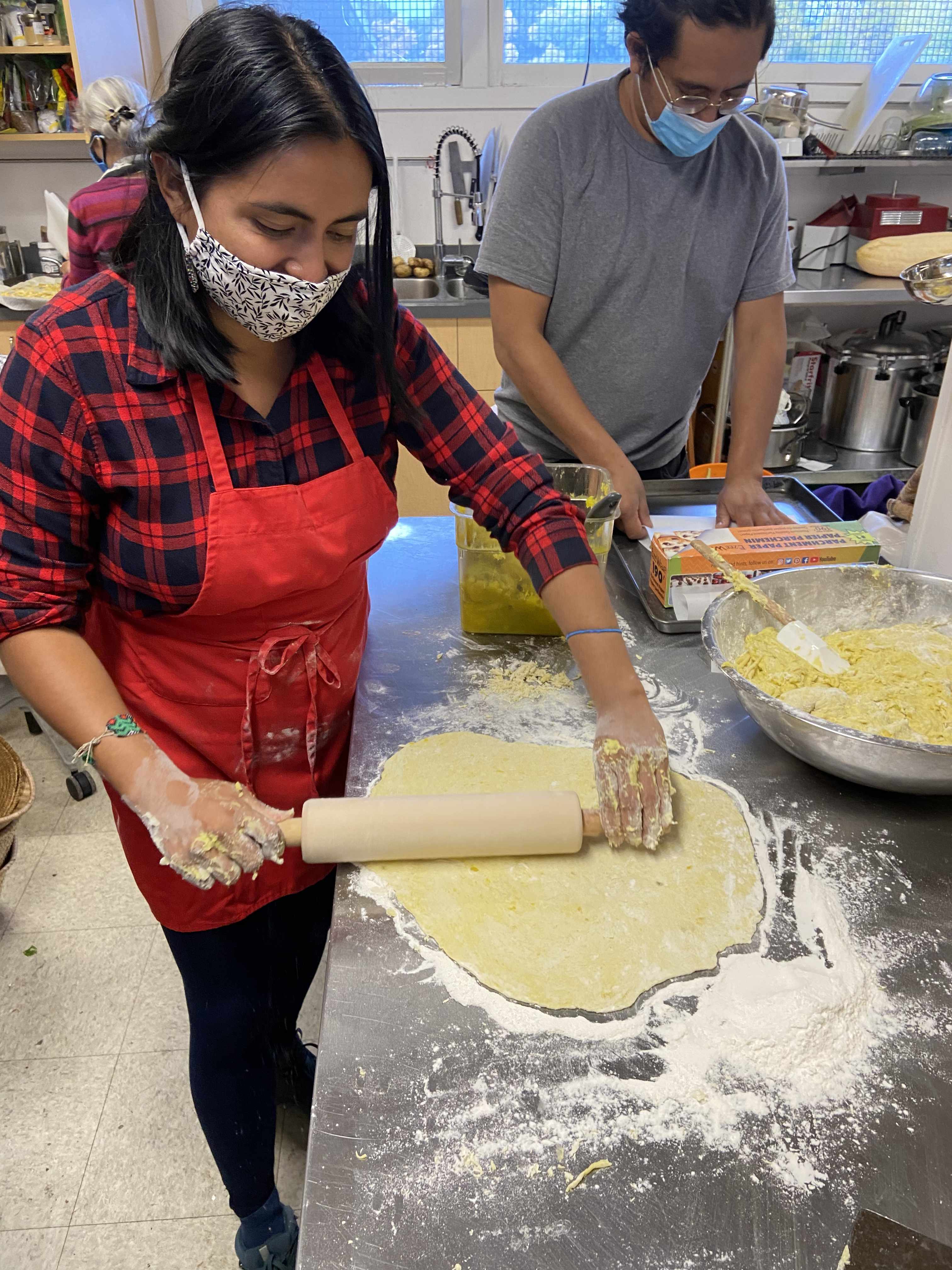 Ingrid rolling the dough with a rolling pin, a smile can be seen coming over her face mask