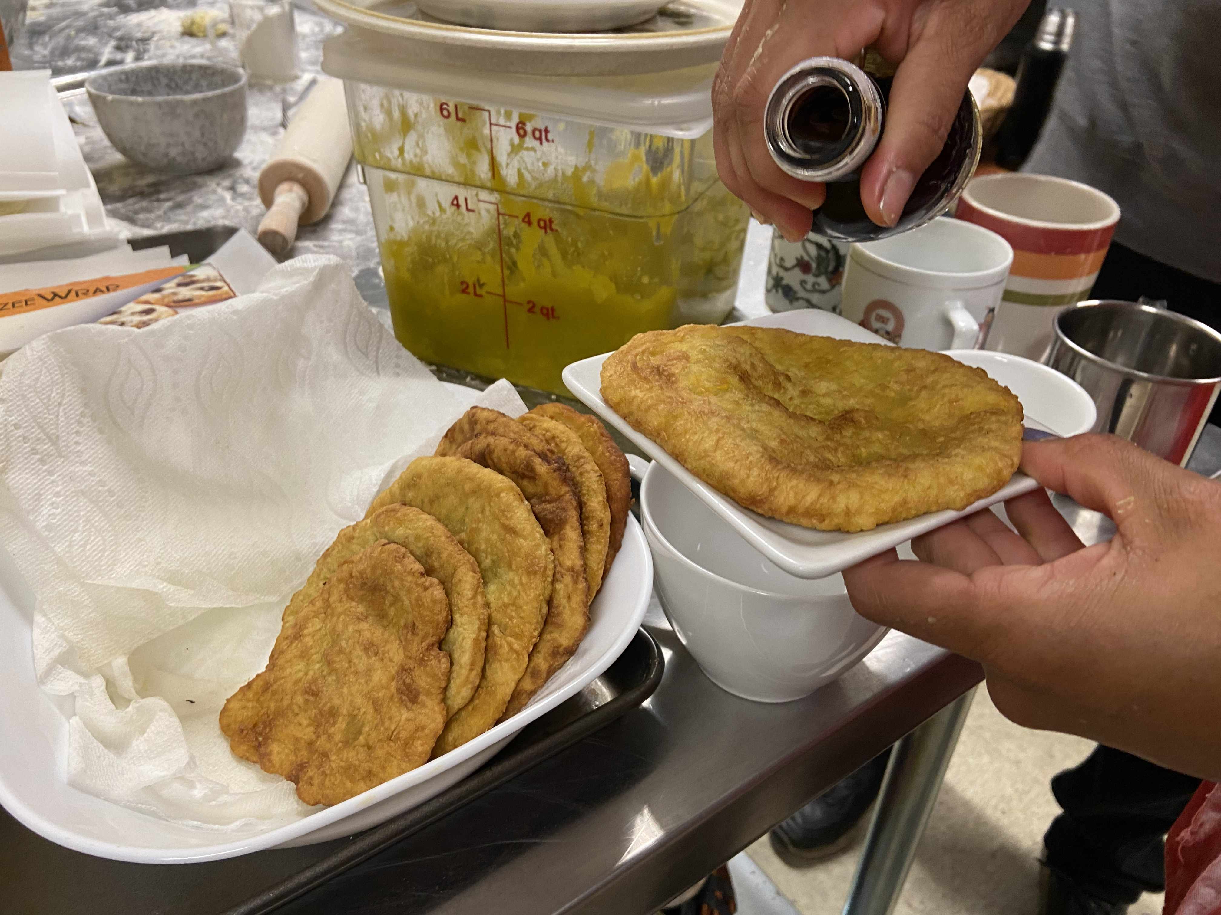 A hand holding a plate of cooked squash bannok alongside a bowl filled with six other finished bannok pieces