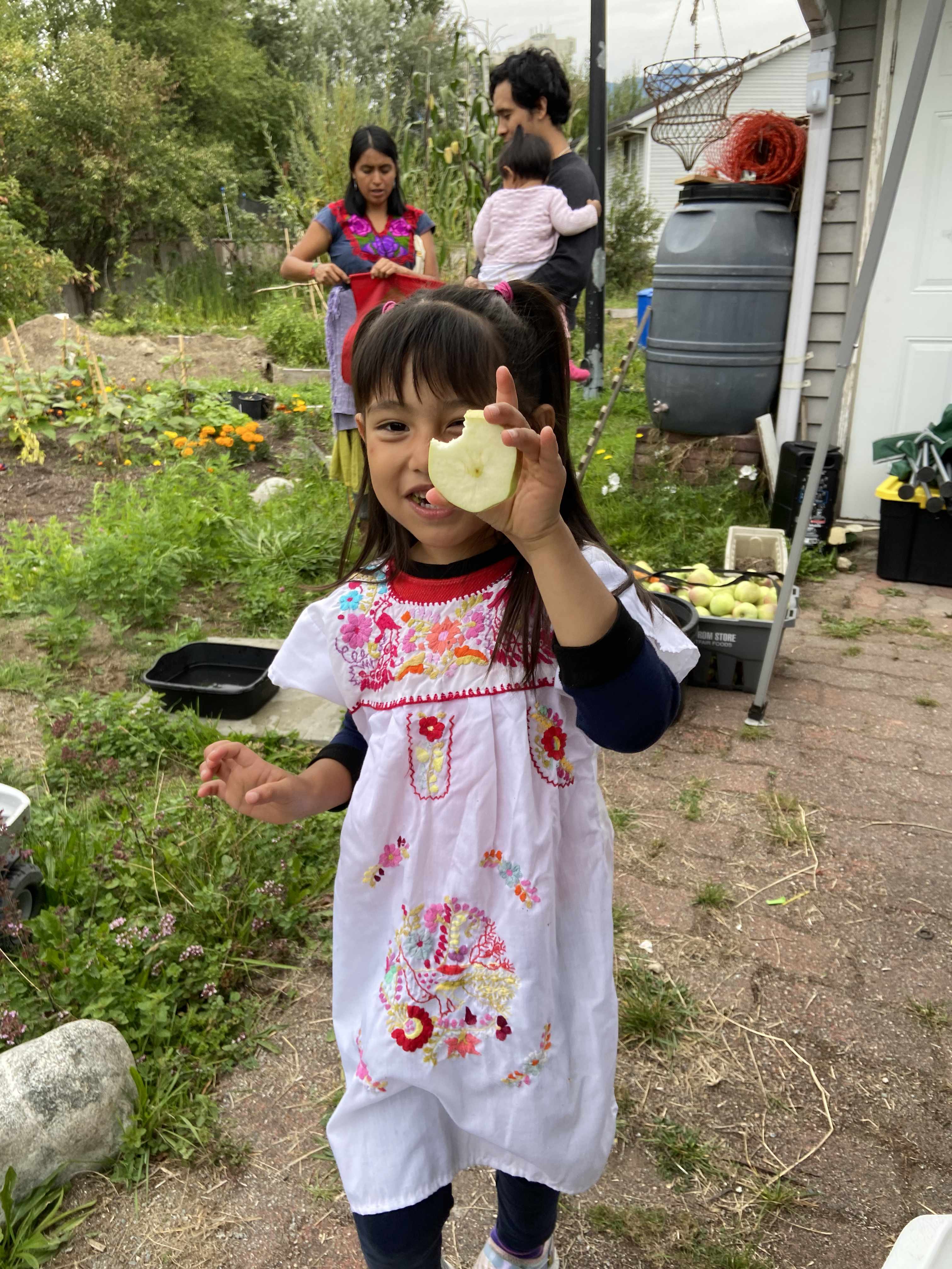 A girl wearing a big smile holding up a slice of apple with a bite taken out of it