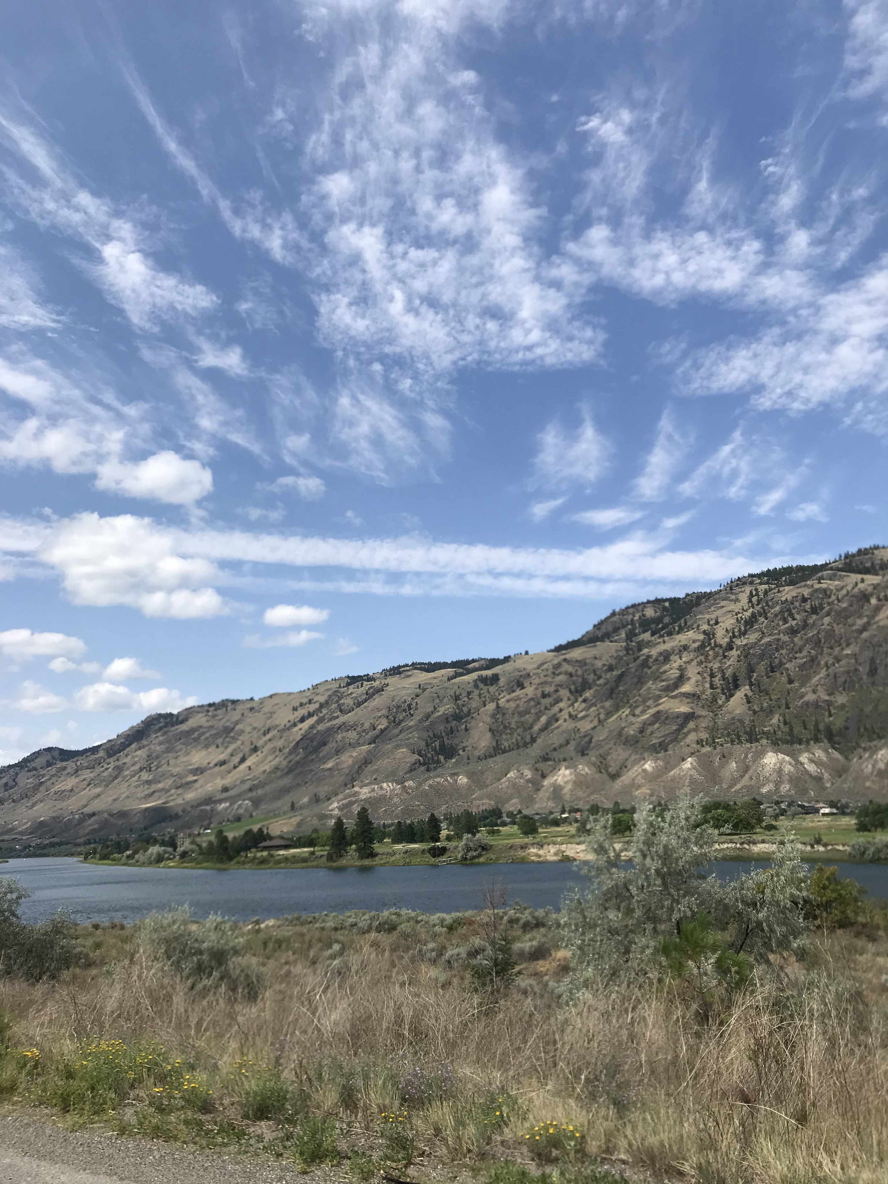 a cloud streaked sky above a rocky terrain with a river running alongside a hill and dry shrubs covering the land