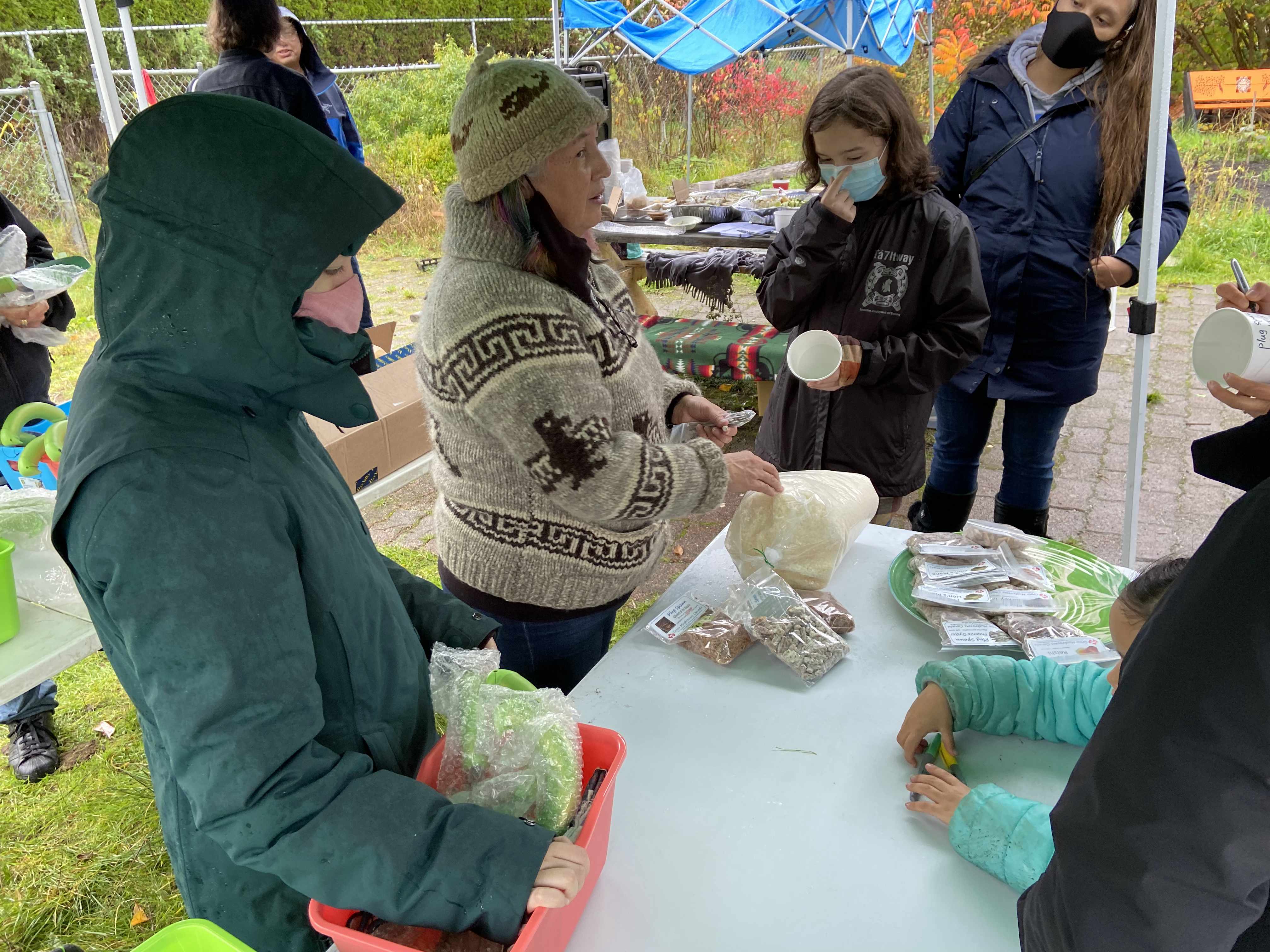 group of people huddled around in the rain under umbrellas choosing plants in pots