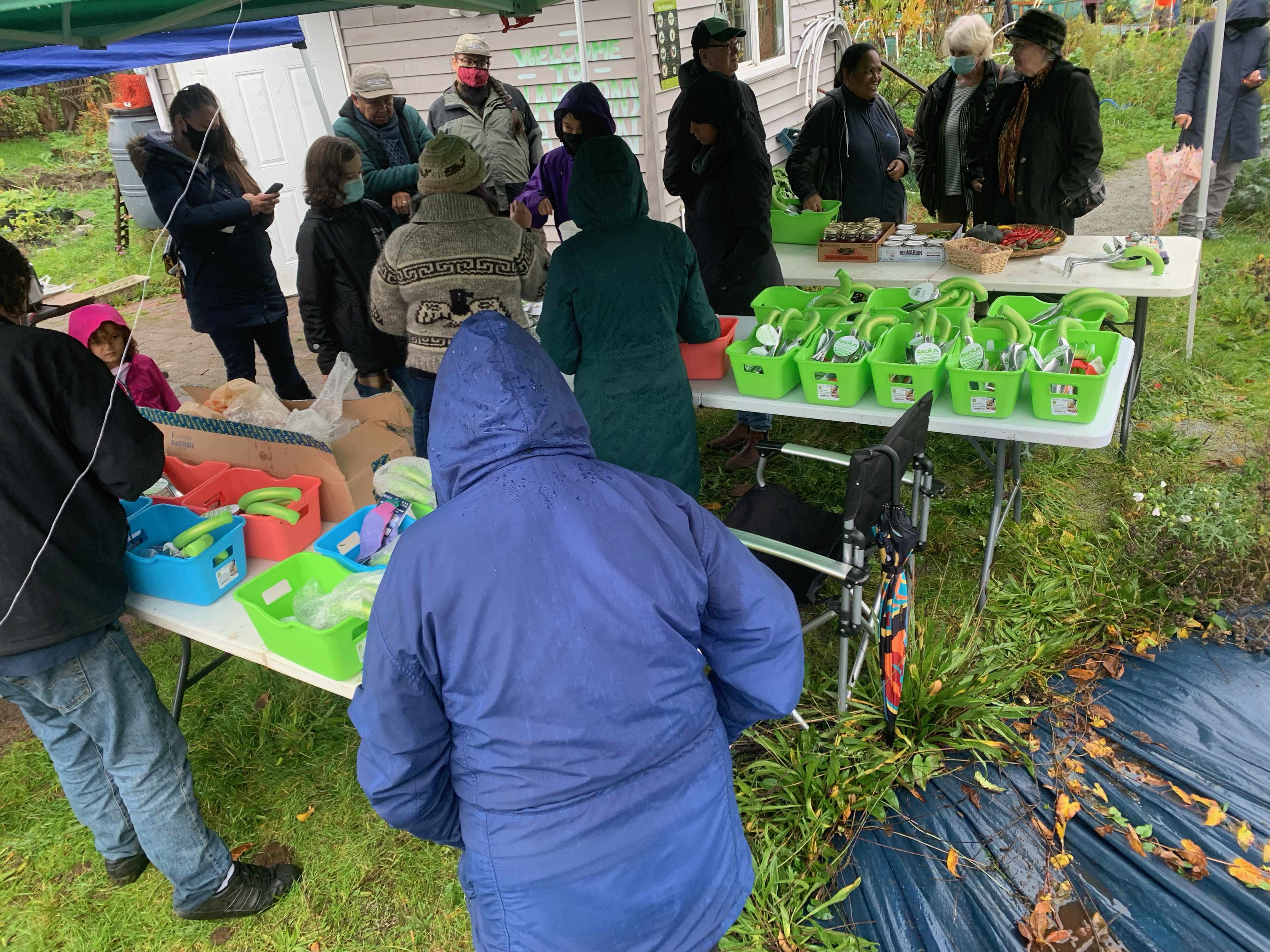 large group of people under a tent outdoors huddled together. everyone is interacting. the tables are full of food and gift baskets